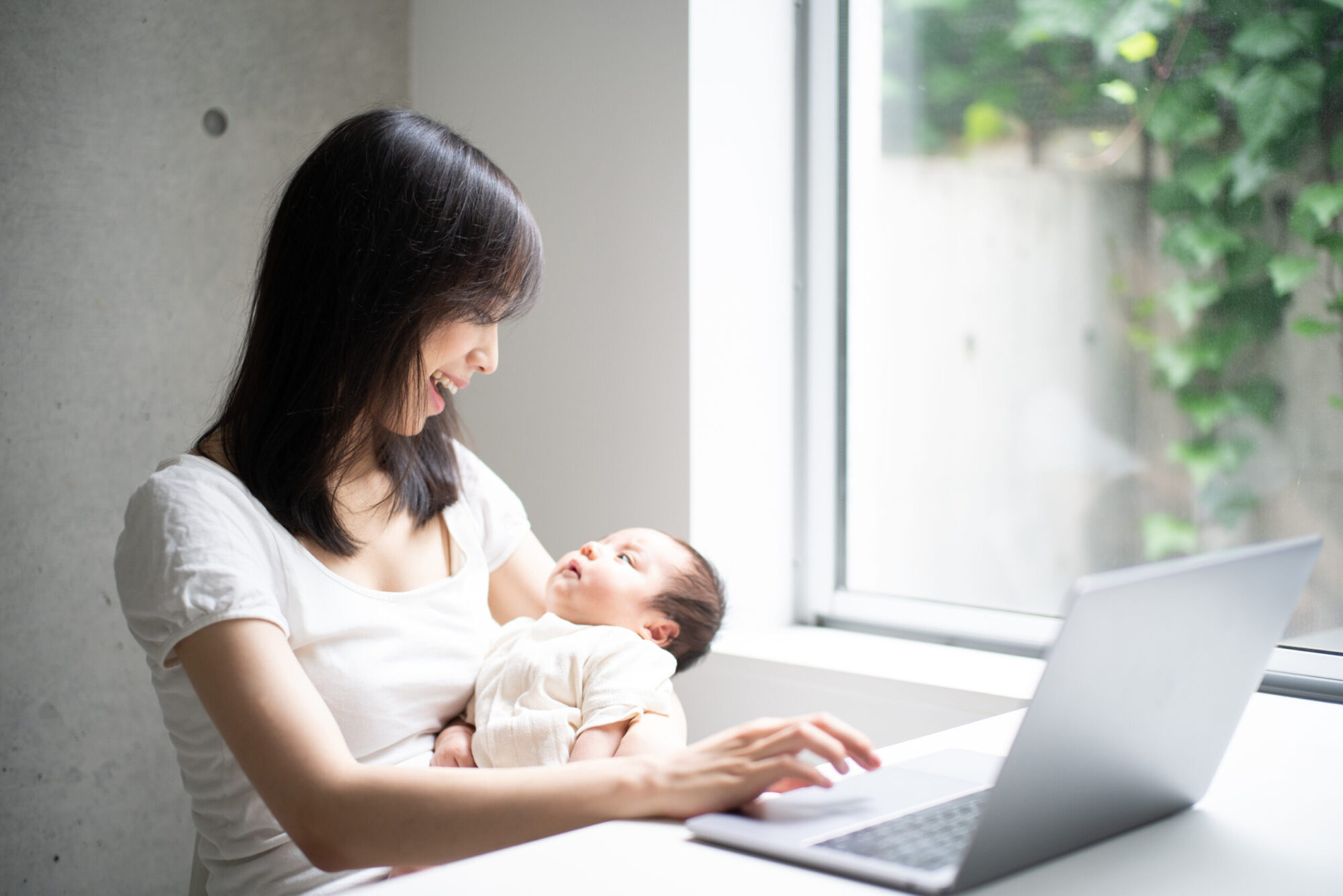 赤ちゃんを抱きながらパソコンを使う女性